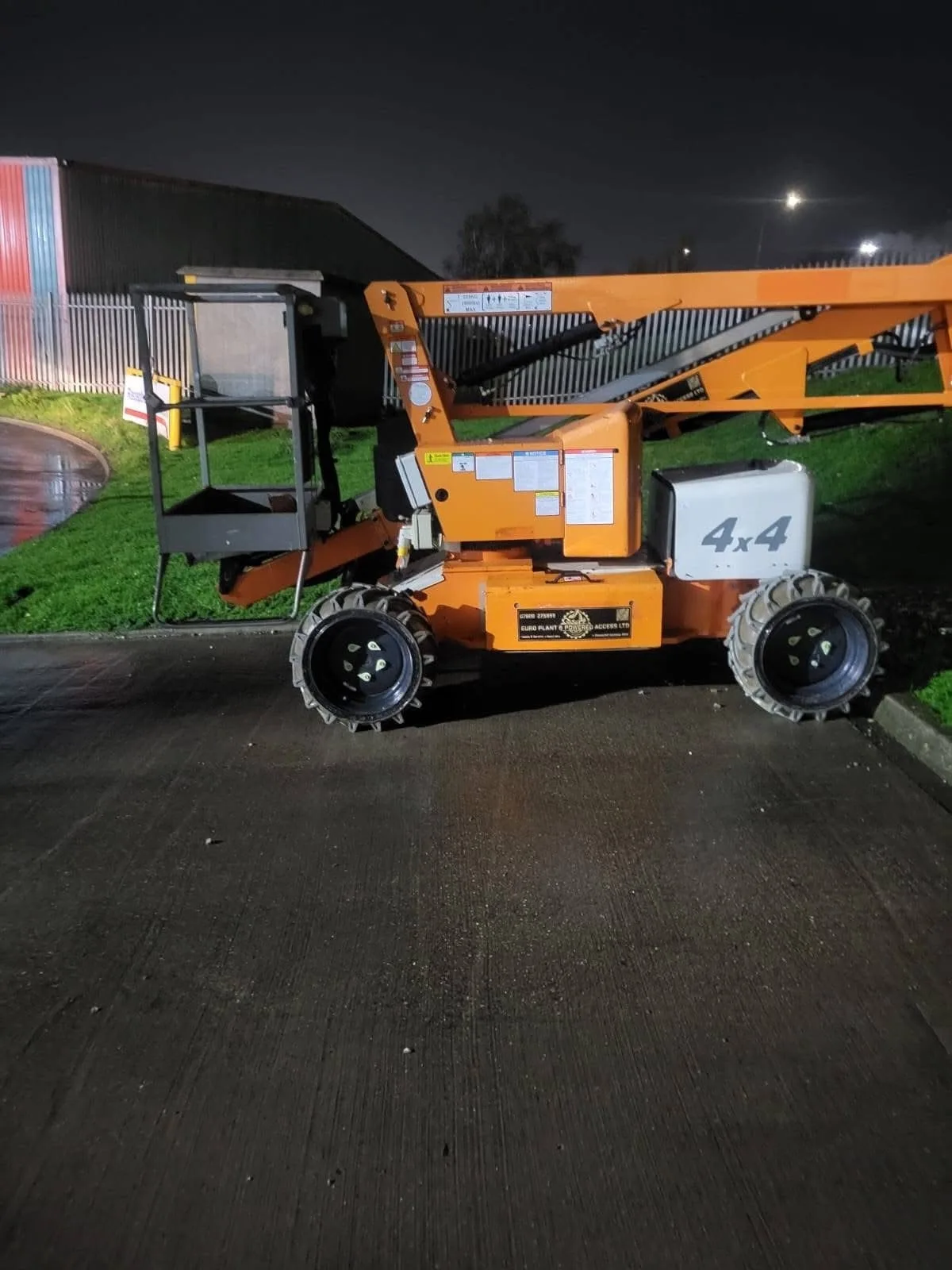 Orange 4x4 boom lift at depot at night